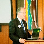 A man in a suit speaks into a microphone on a podium
